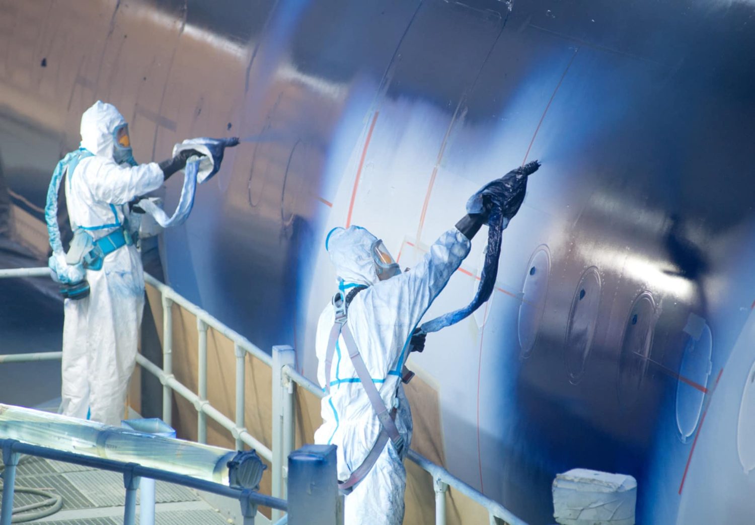 Workers manually spray-painting a large structure